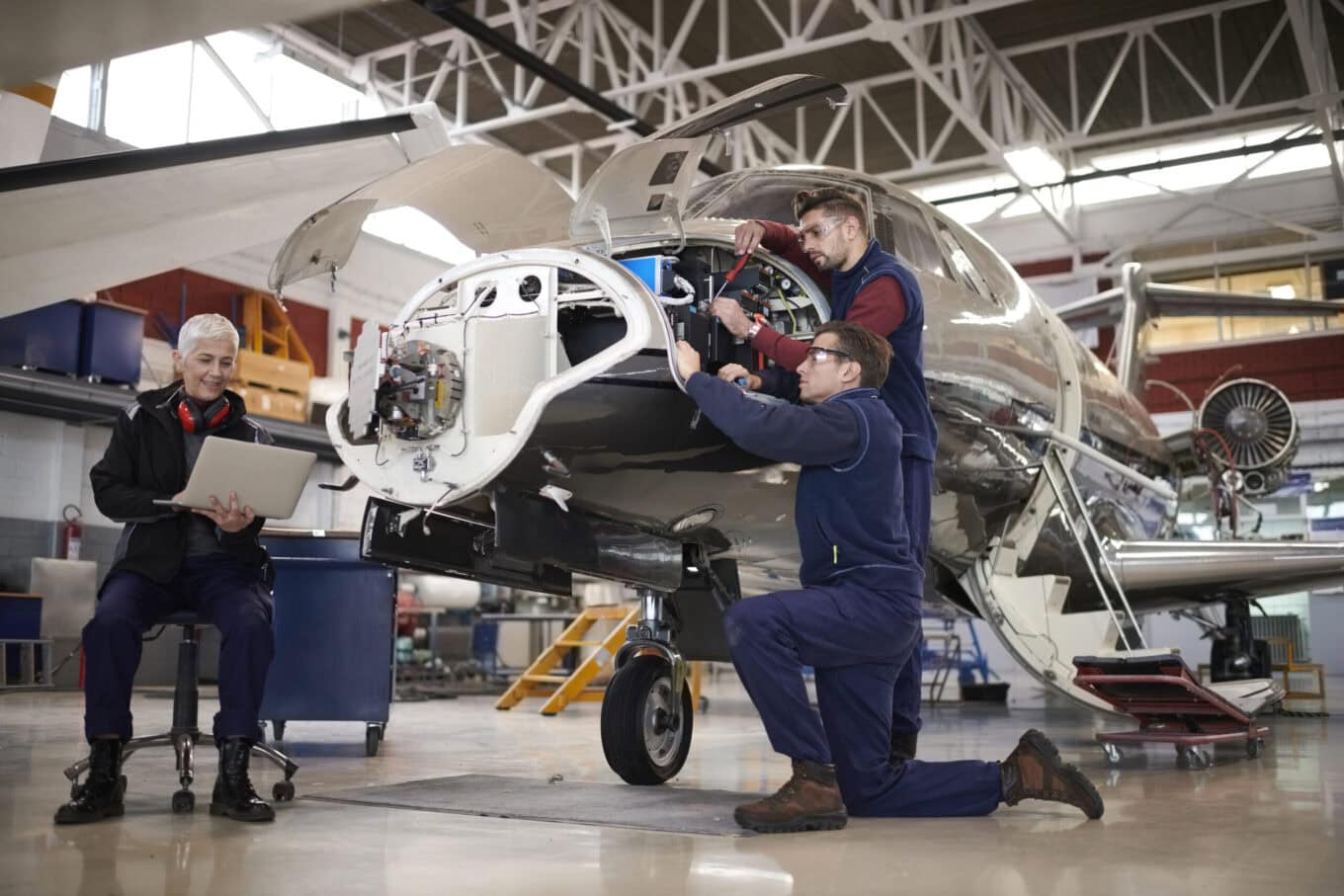 Dos técnicos y una ingeniera trabajan en un avión en el hangar para llevar a cabo tareas de mantenimiento y reparación, en el marco de un servicio de selección de personal para el sector aeronáutico.