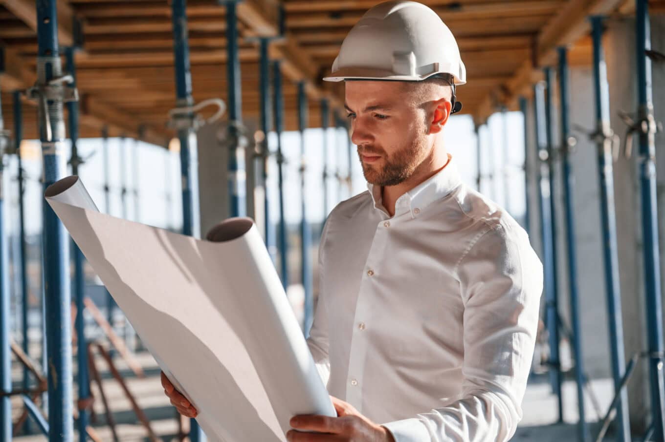 Bauleiter mit Helm prüft Baupläne auf einer Baustelle, um Qualität und Fortschritt zu sichern. Professionelle Personalvermittlung für Bau- und Projektmanagement.
