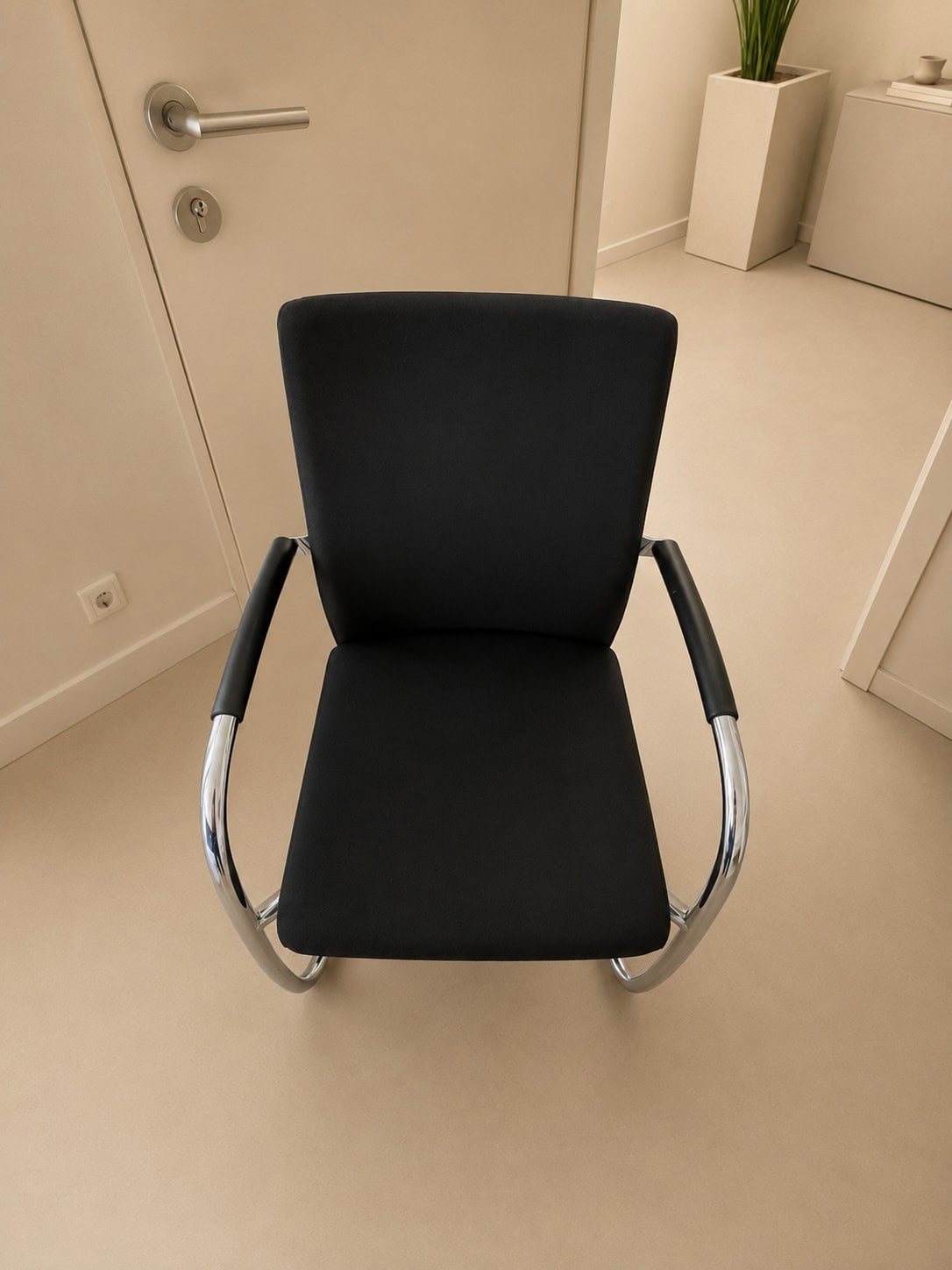 Scaun de birou modern, negru, cu cotiere metalice, destinat unui birou sau unei săli de așteptare, confortabil și cu un design ergonomic.